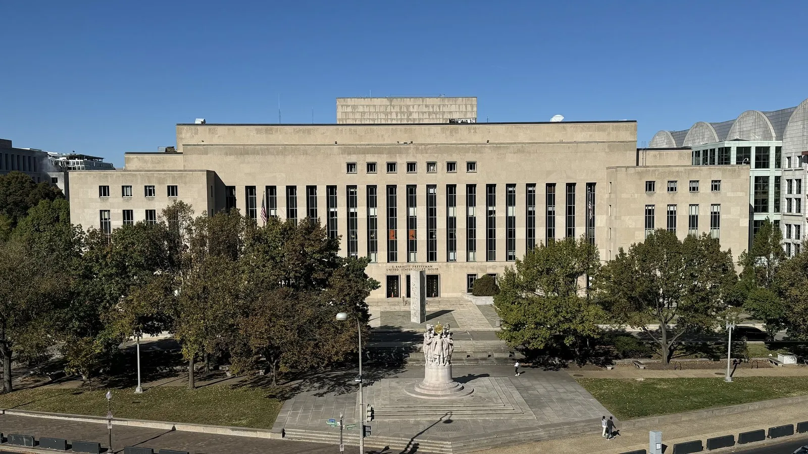 Facciata in pietra chiara del tribunale federale E. Barrett Prettyman a Washington, con alberi e un monumento in primo piano sotto un cielo azzurro