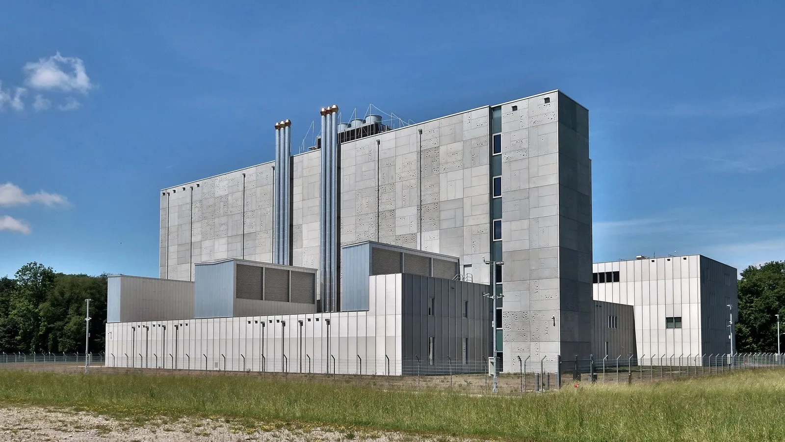 Edificio grigio in cemento di un data center, con camini di sfiato e recinzione di sicurezza, sotto un cielo azzurro.