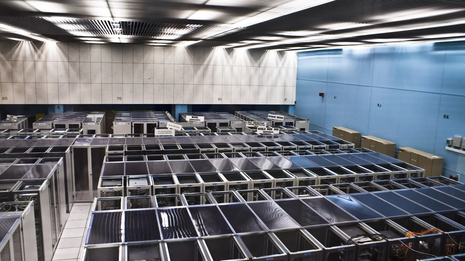 Ein großer Serverraum von oben, mit Reihen von Server-Racks und Schildern für Mail-Server und Webserver.
